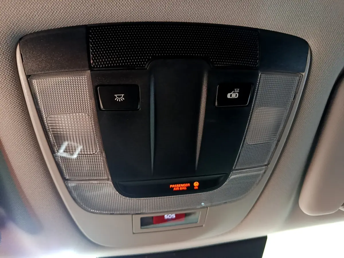 Vue en contre-plongée du plafonnier noir et gris avec boutons d'éclairage et témoin airbag passager allumé du Kia Sportage blanc hybride.