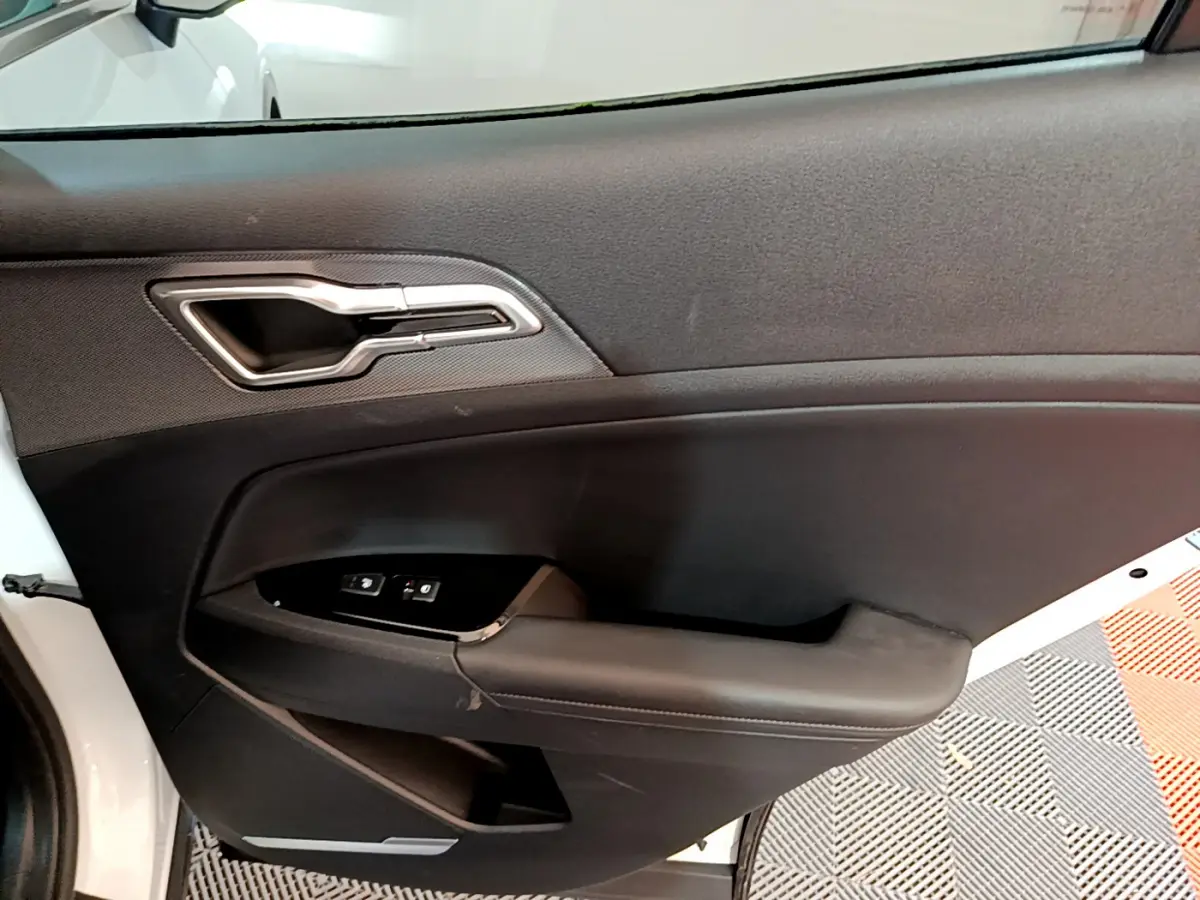 Vue intérieure de la porte côté conducteur du KIA SPORTAGE blanc 2022 avec poignée argentée et commandes vitres.