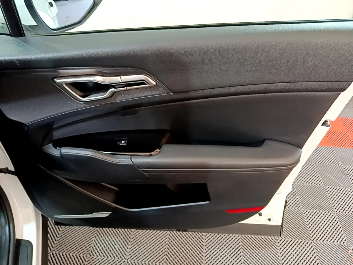 Vue intérieure côté gauche de la porte avant blanche du Kia Sportage 2022 avec poignée argentée et panneau noir.