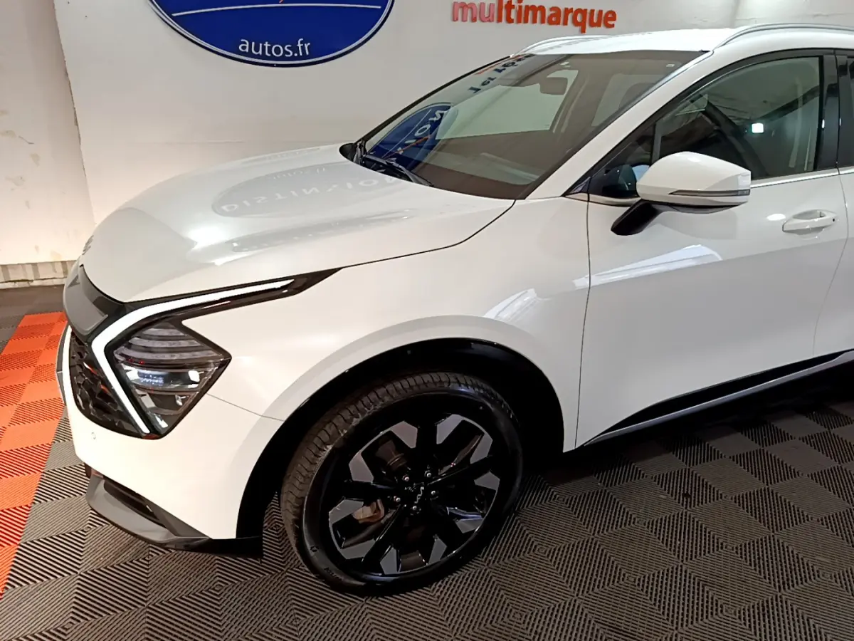 Vue 3/4 avant droit du KIA SPORTAGE blanc avec jantes noires et feux avant LED distinctifs.