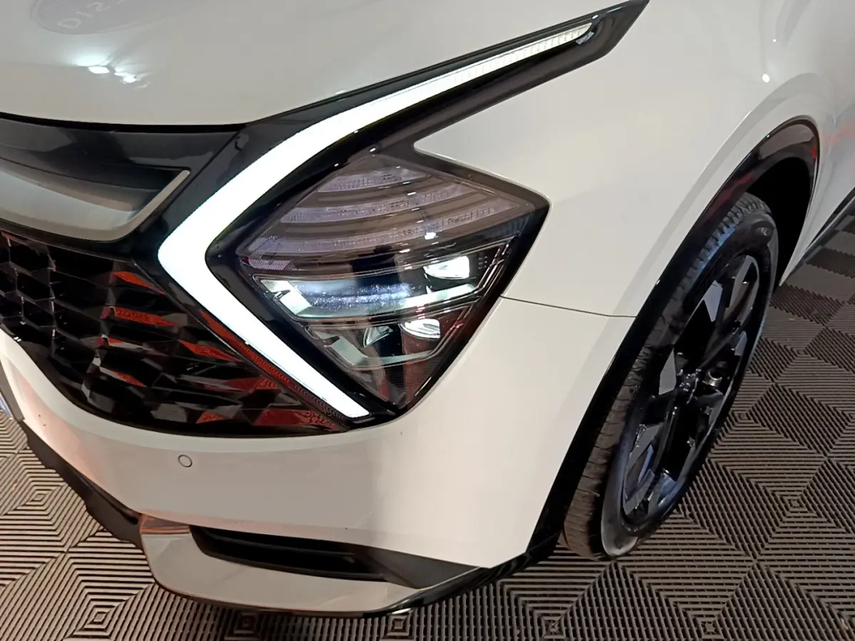Gros plan sur le phare avant droit blanc du KIA SPORTAGE 2022 avec éclairage LED et jante noire visible.