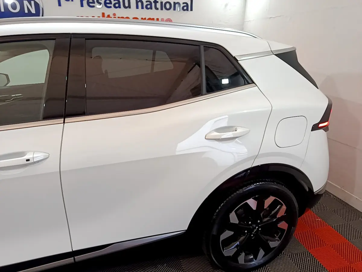 Vue latérale droite du KIA SPORTAGE blanc 2022 avec jantes noires et feux arrière LED allumés.