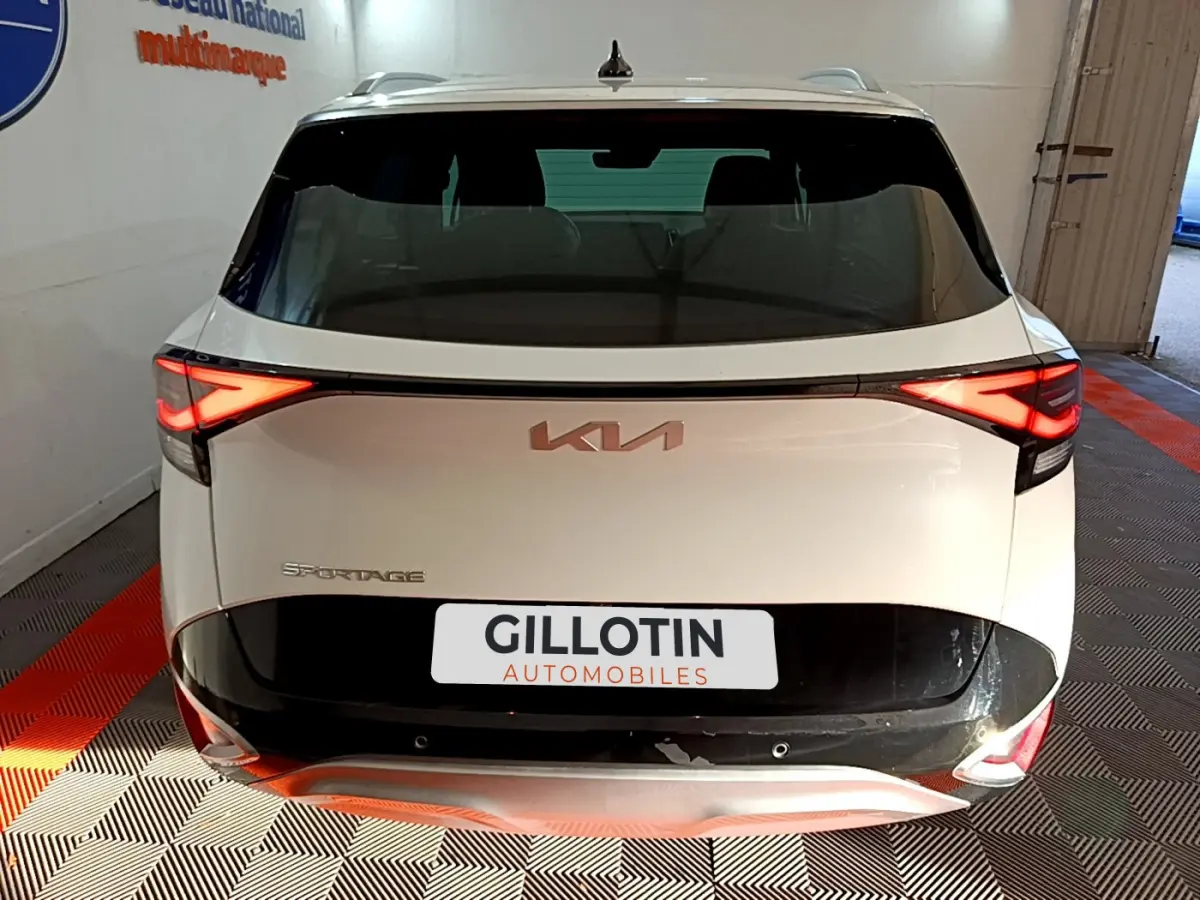 Vue arrière d'un KIA SPORTAGE blanc 2022 avec feux LED allumés et logo KIA visible sur le hayon noir.