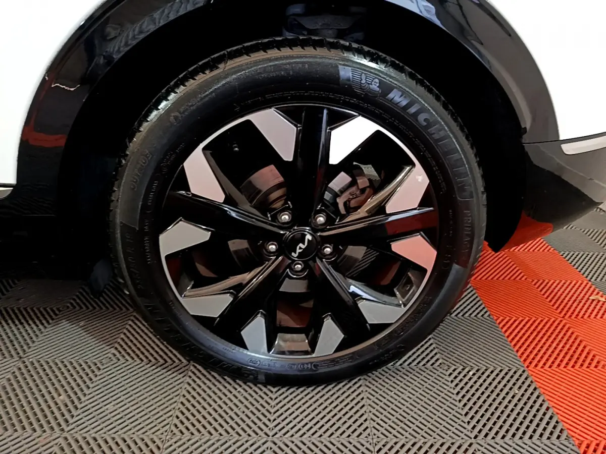 Gros plan sur la roue avant gauche du Kia Sportage blanc 2022, mettant en valeur la jante noire brillante au design moderne.