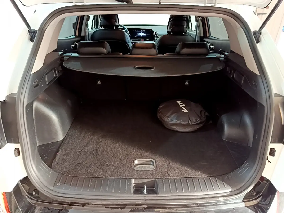 Coffre ouvert d'un KIA SPORTAGE blanc 2022, vue arrière, avec housse ronde noire au sol et banquette arrière visible.