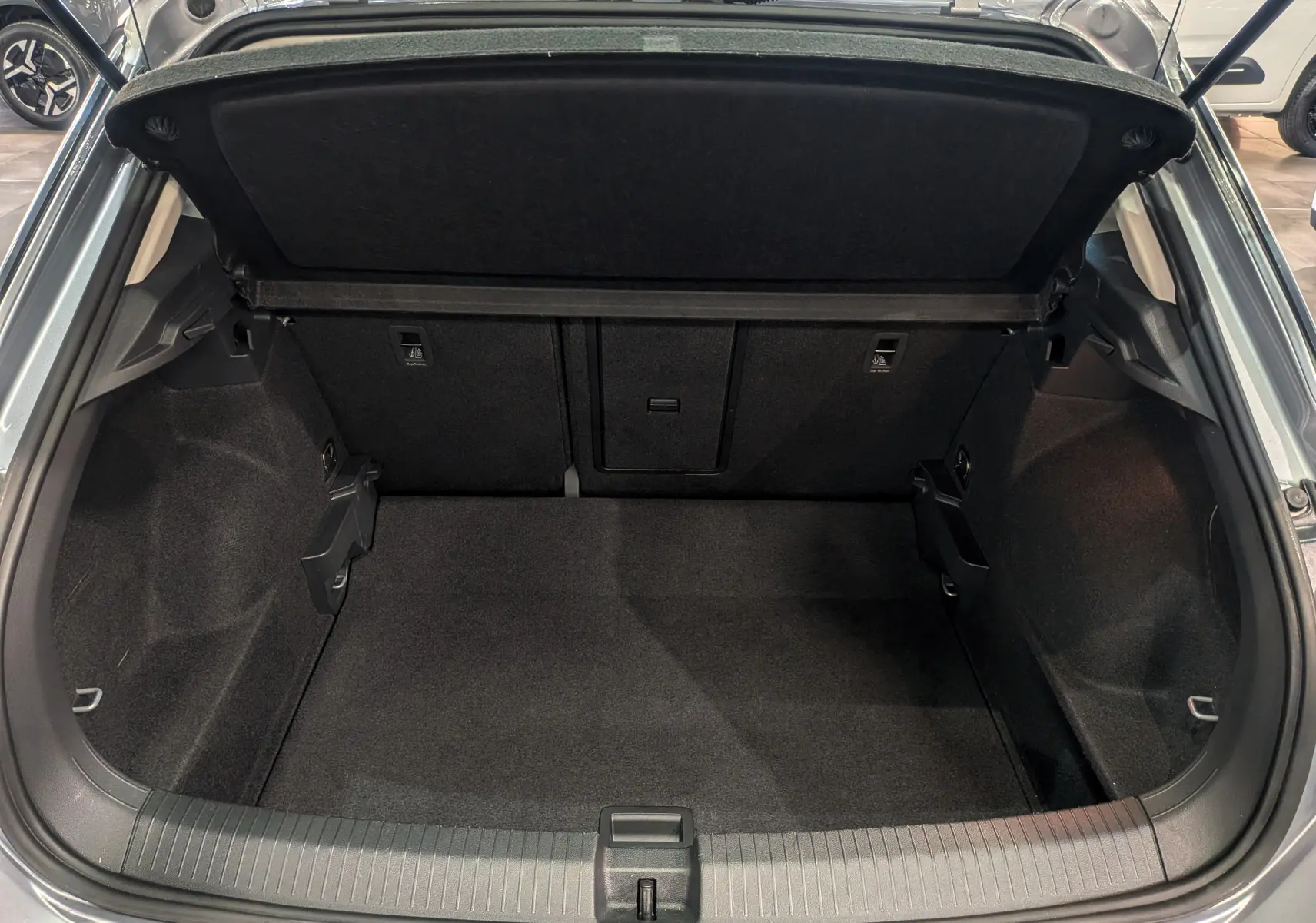 Coffre ouvert vu de l'arrière d'un Volkswagen T-Roc gris pyrite, montrant un espace de chargement propre et spacieux.
