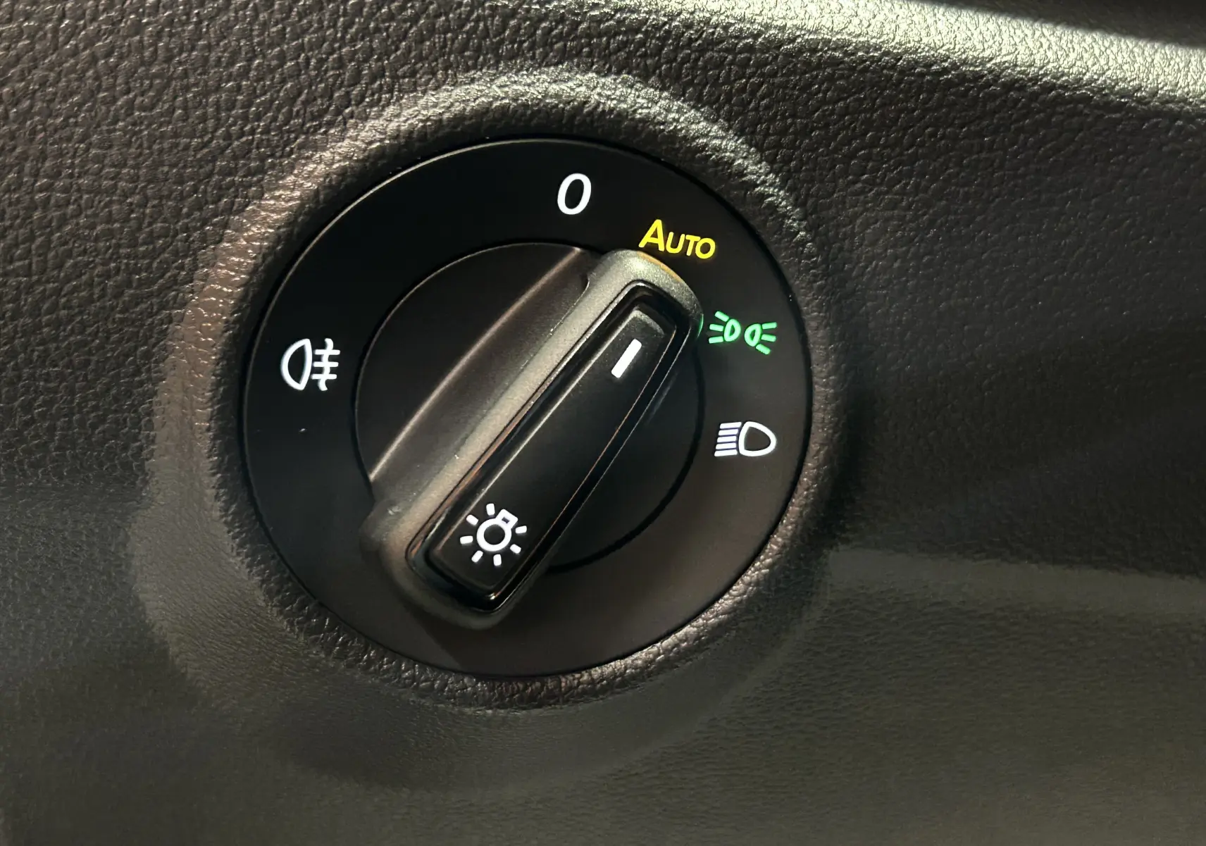 Gros plan sur le sélecteur de phares du Volkswagen T-Roc 2025, avec mode automatique activé, sur tableau de bord noir.