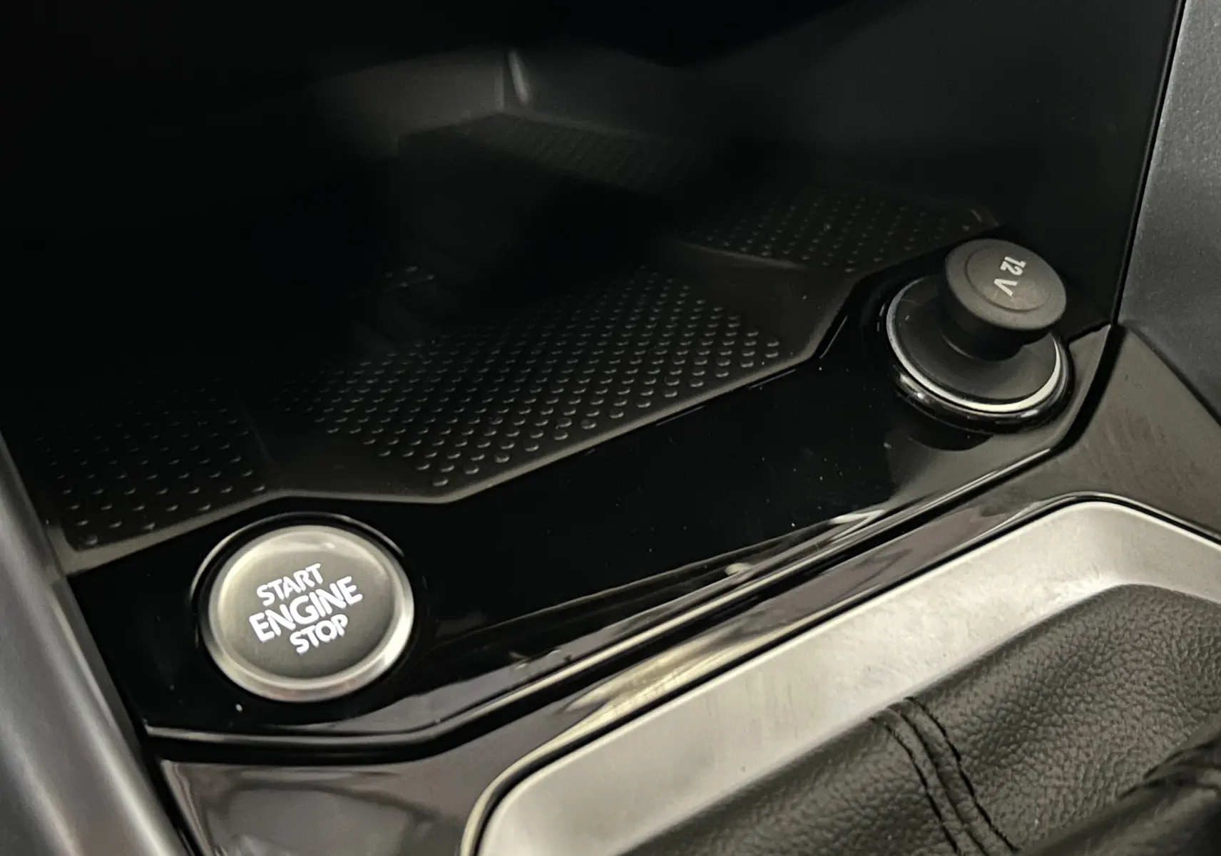 Gros plan sur la console centrale du Volkswagen T-Roc 2025, bouton Start Engine Stop et prise 12V sur finition noire brillante.