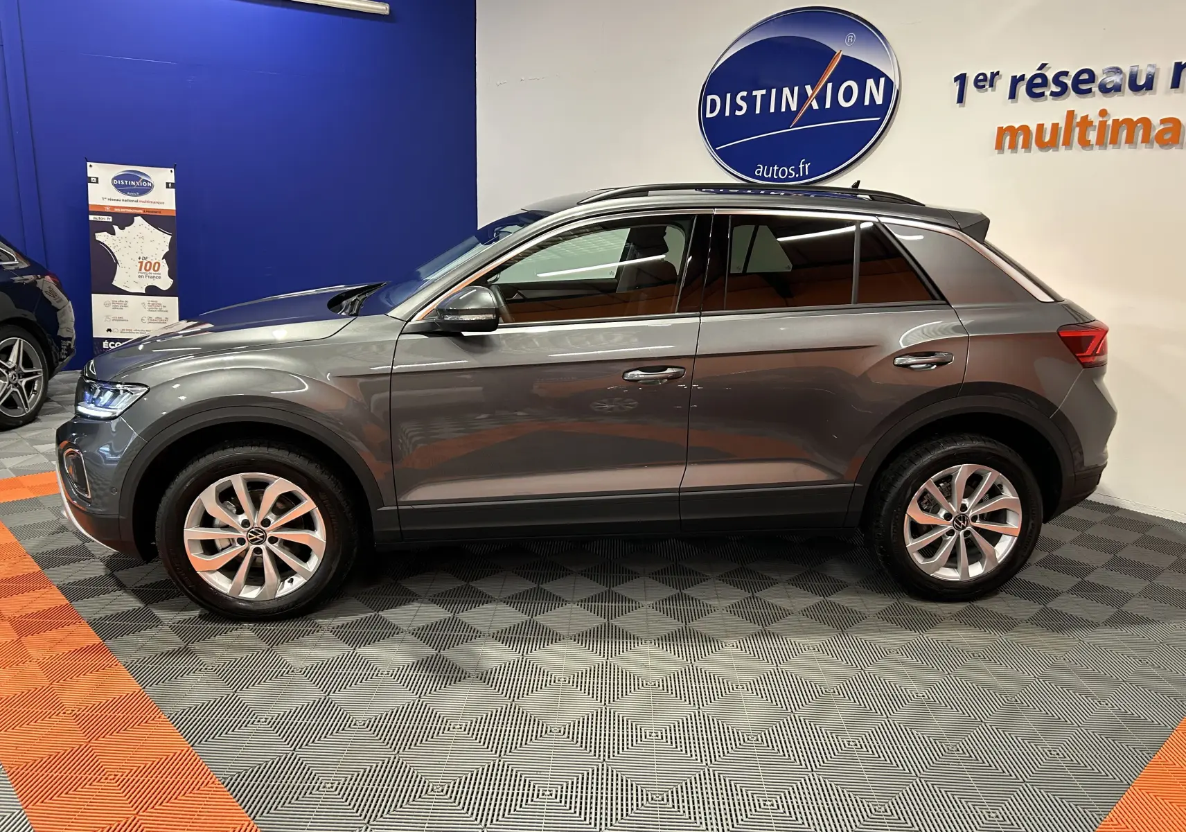 Profil droit d'un Volkswagen T-Roc gris Indium Metal 2025 en showroom, avec jantes alliage et vitres teintées.
