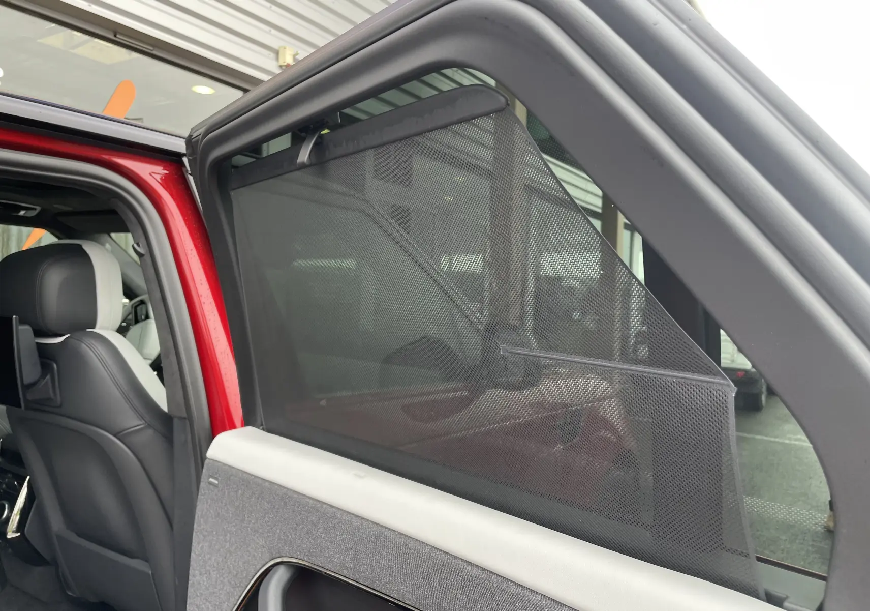 Vue intérieure côté gauche arrière du Range Rover Sport P440 HSE R-Dynamic rouge Italian Racing avec pare-soleil en filet déployé.