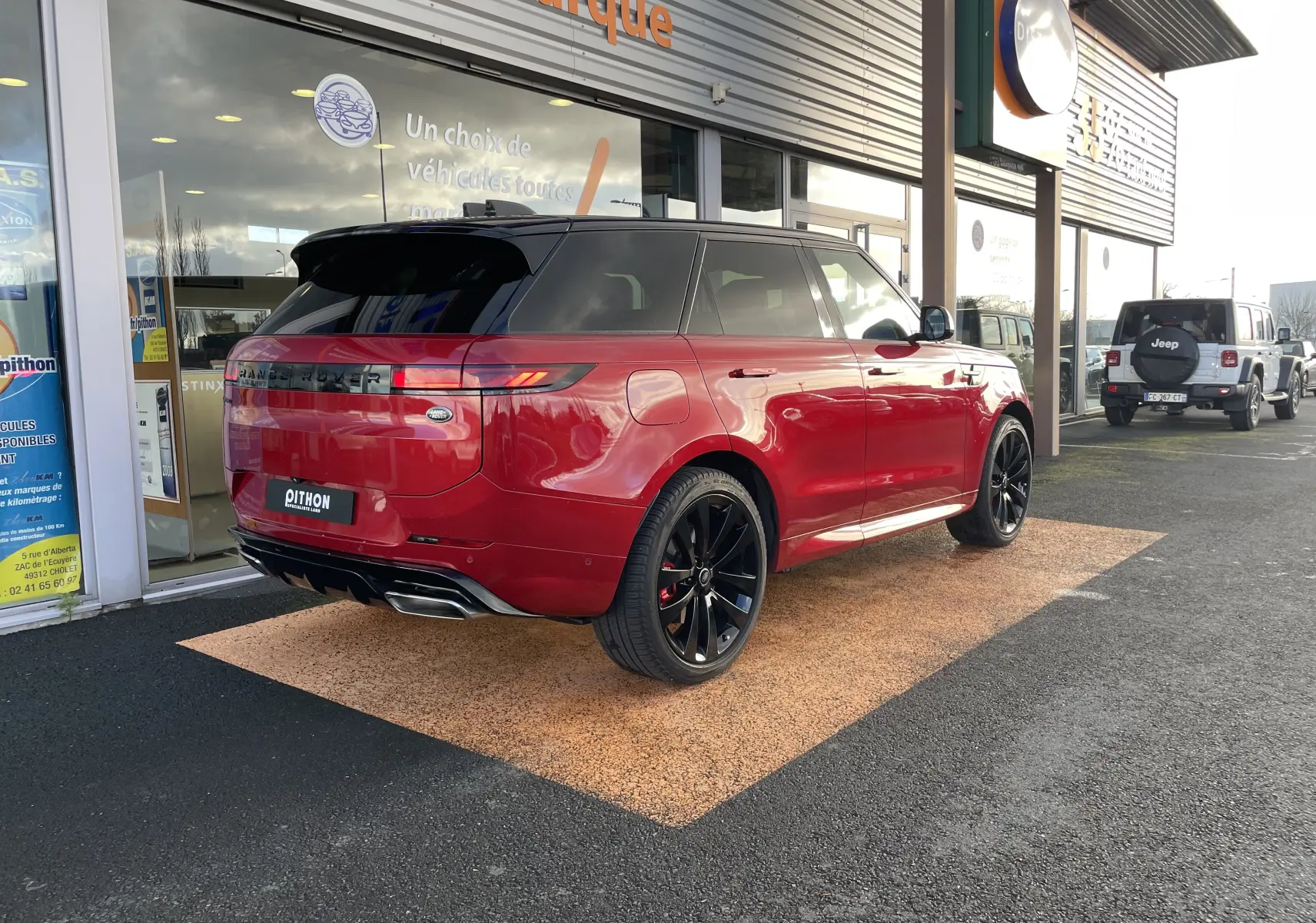 Vue 3/4 arrière droite d'un Range Rover Sport P440 HSE R-Dynamic rouge Italian Racing avec toit noir et jantes noires 23 pouces.