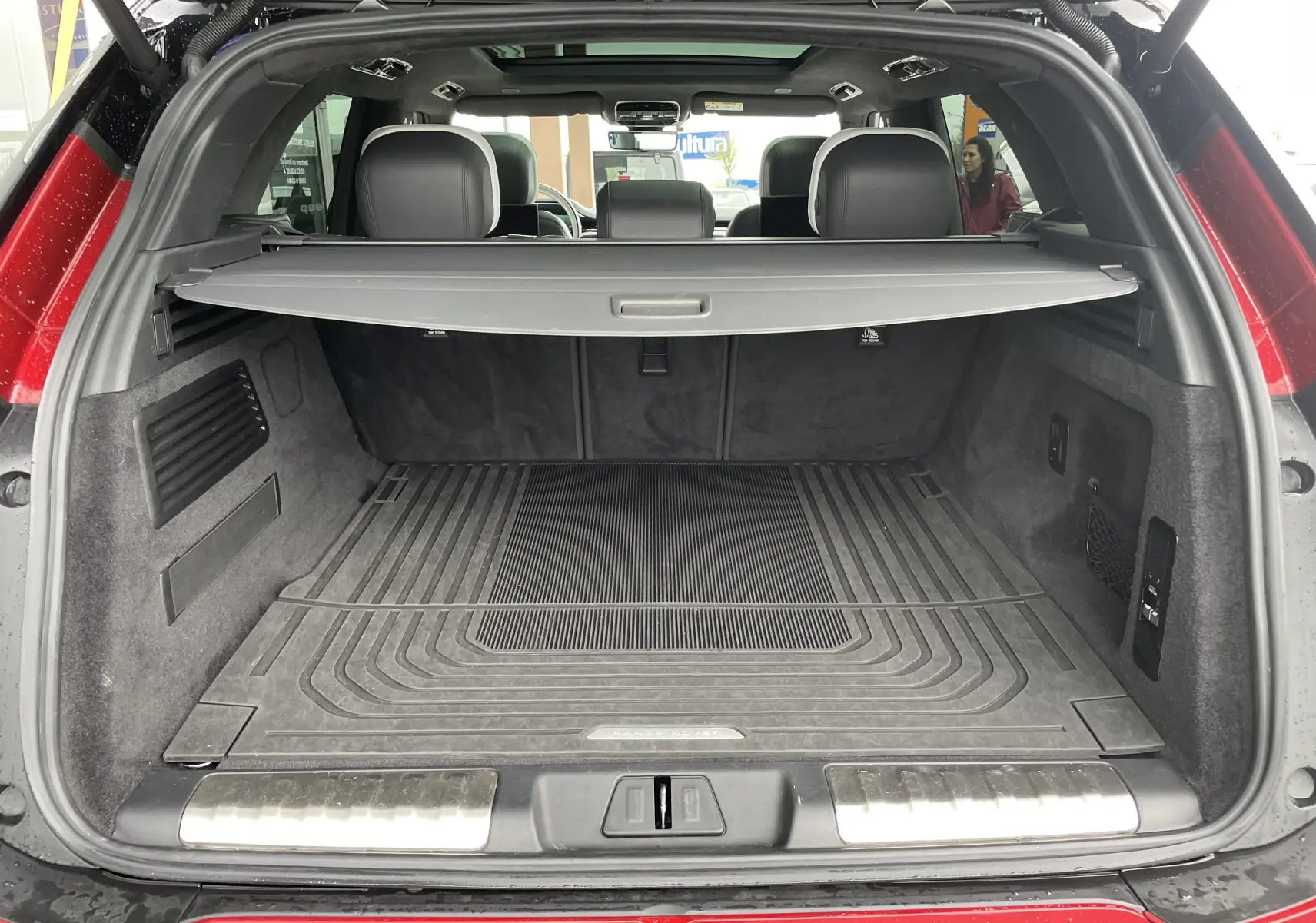 Coffre ouvert vu de l'arrière d'un Range Rover Sport P440 HSE R-Dynamic rouge Italian Racing avec tapis de sol et cache-bagages.