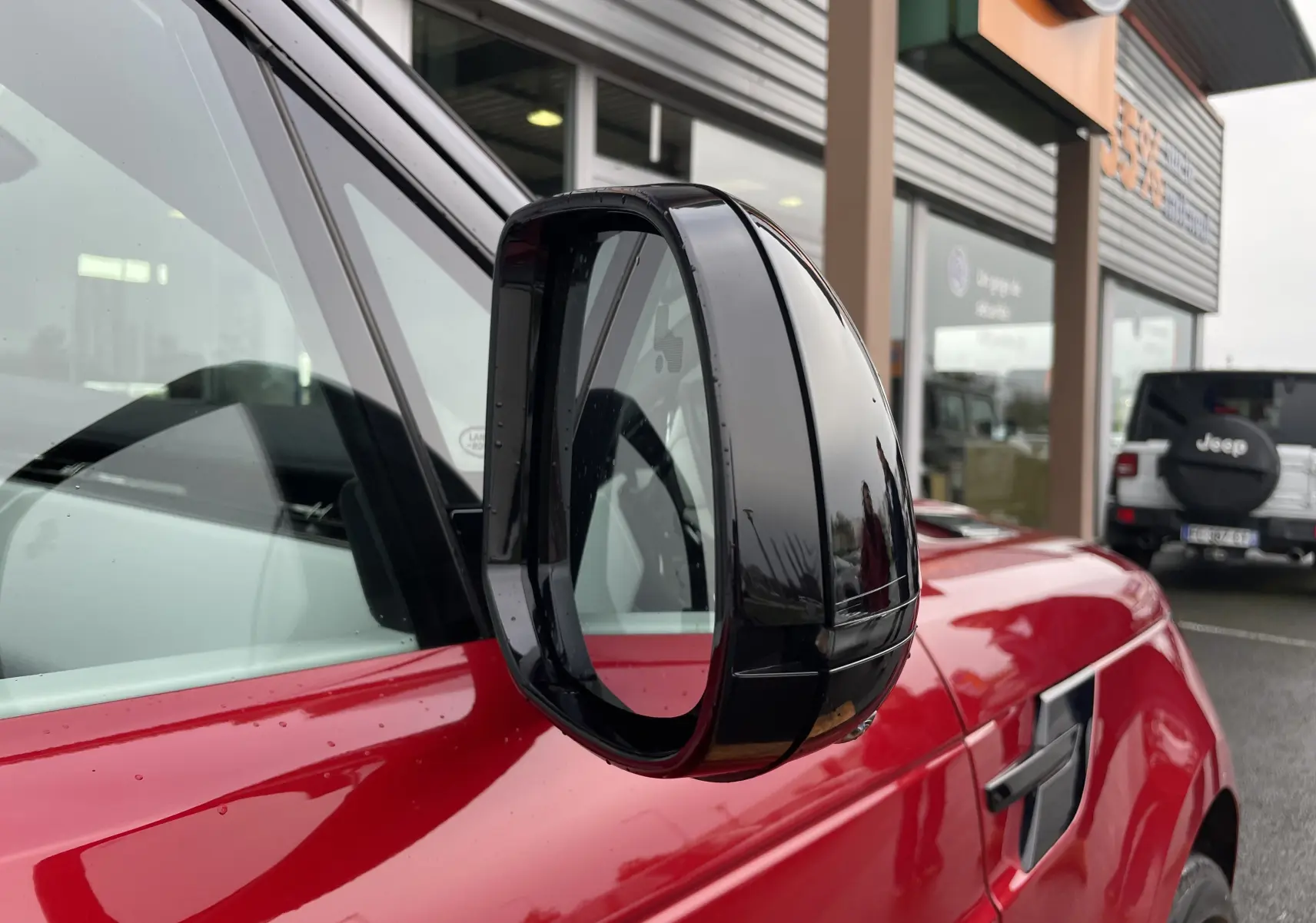 Rétroviseur noir en gros plan côté gauche du Range Rover Sport P440 HSE R-Dynamic rouge Italian Racing, vue avant.