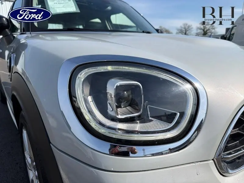 Gros plan sur le phare avant droit du MINI Countryman Cooper SE Moonwalk Grey, soulignant le contour chromé et la carrosserie claire.
