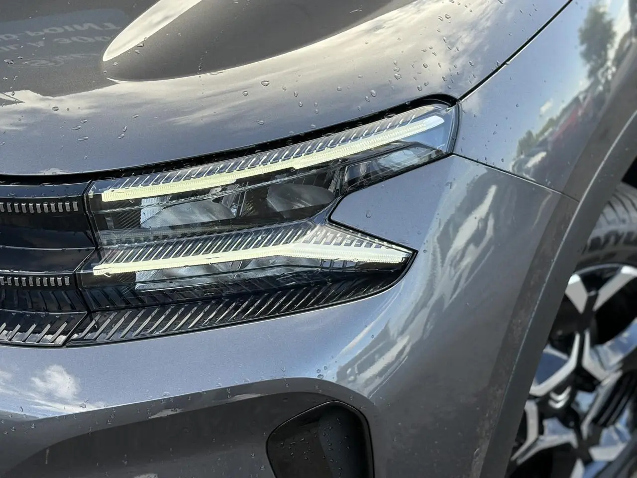 Gros plan sur le phare avant droit allumé du Citroën C5 Aircross 2025 gris Platinium avec jante alliage visible