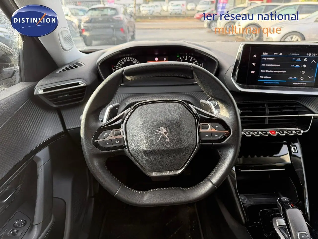Vue intérieure centrée sur le volant cuir noir et le tableau de bord numérique du Peugeot 2008 gris Artense 2022.