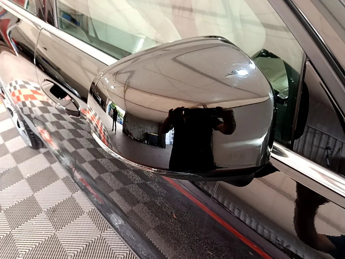 Rétroviseur côté gauche noir brillant d'un Volvo XC40 T3 2020, reflétant l'intérieur d'un garage avec sol damier.