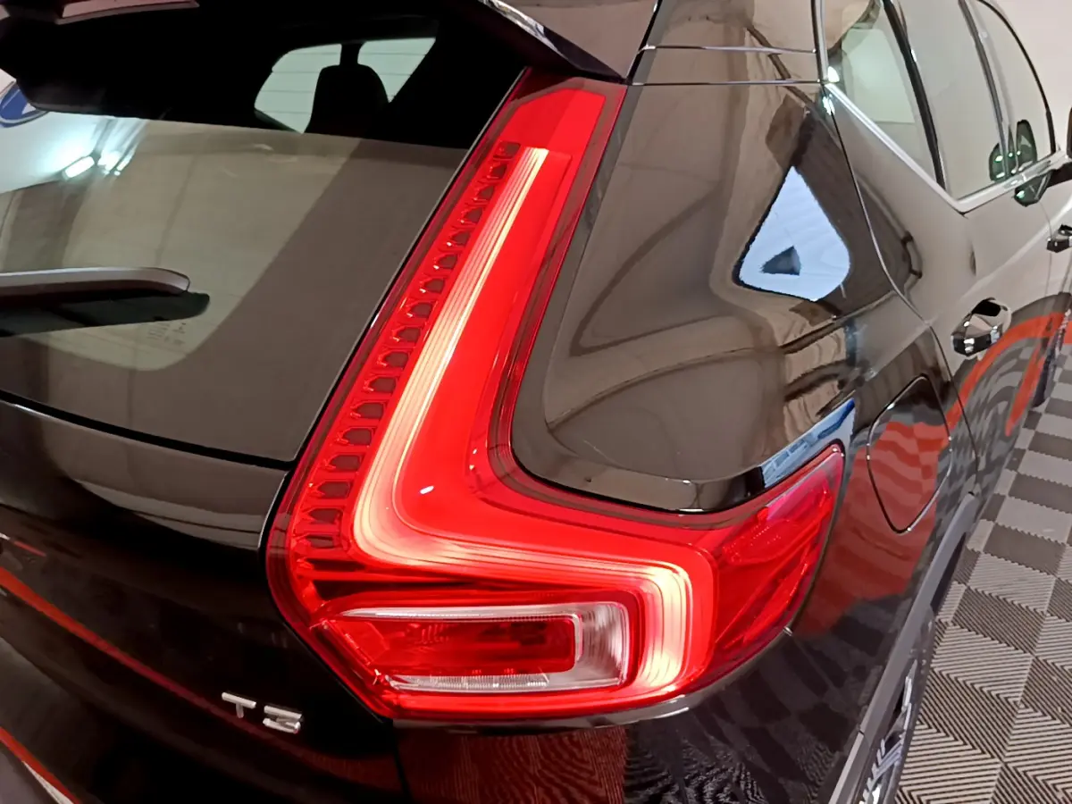 Gros plan sur le feu arrière droit allumé d’un Volvo XC40 T3 noir, reflétant l’éclairage intérieur du garage.