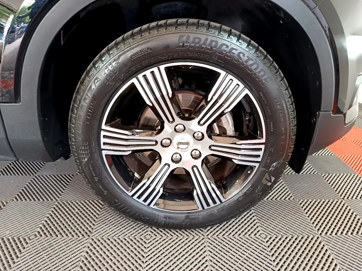 Gros plan sur la roue avant droite du Volvo XC40 noir, mettant en valeur la jante alliage à rayures argentées et pneus Bridgestone.