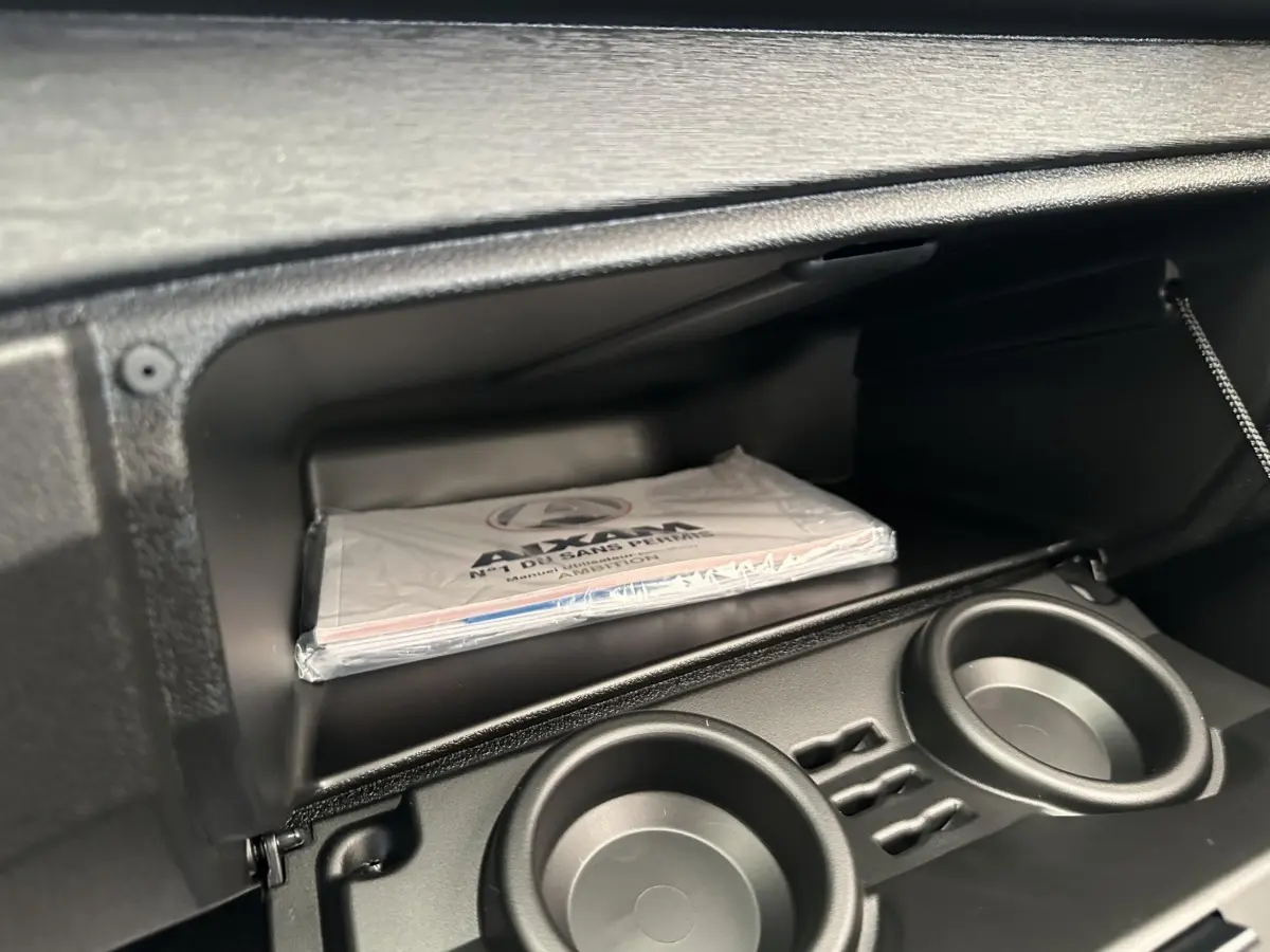 Intérieur de la boîte à gants de l'AIXAM AMBITION 0.5 CITY PACK 2026, avec manuel et porte-gobelets noirs.
