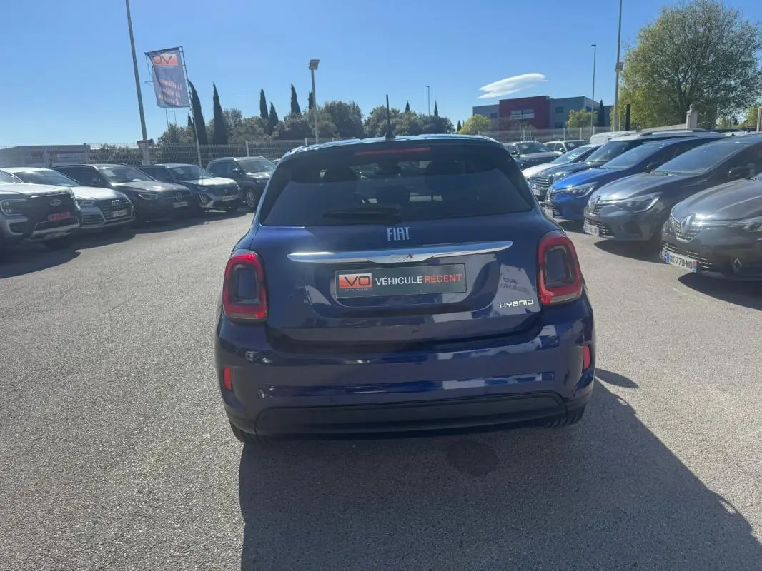 Vue arrière d'une FIAT 500X bleu foncé avec feux arrière distinctifs et badge hybride visible sur un parking.