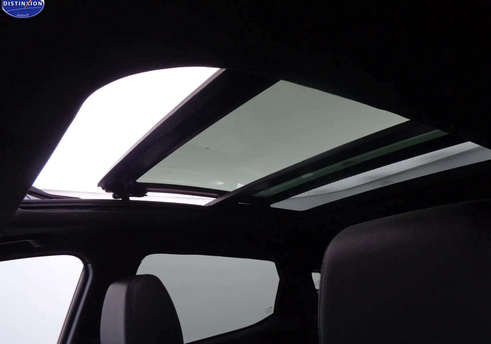 Toit panoramique ouvert vu de l'intérieur du SERES 3 électrique, mettant en valeur l'habitacle sombre et les sièges noirs.