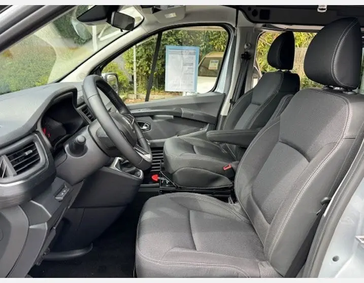 Intérieur côté conducteur du Renault Trafic Fourgon gris Highland, sièges noirs avec accoudoirs pivotants et tableau de bord moderne.