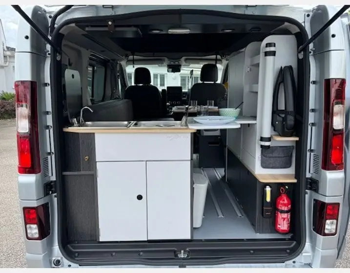 Vue arrière ouverte du Renault Trafic Fourgon gris Highland montrant l'aménagement intérieur cuisine et rangements.