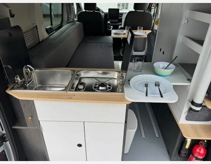 Intérieur du Renault Trafic Fourgon Antilope Van Flex Plus, vue cuisine équipée avec évier, réchaud et table dépliée.