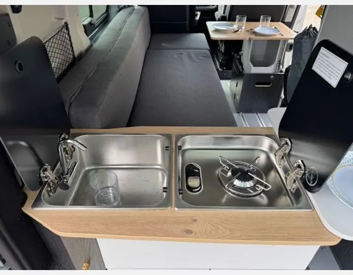 Cuisine intégrée avec évier inox et réchaud gaz dans l'aménagement intérieur gris du Renault Trafic Fourgon Antilope Van Flex Plus.