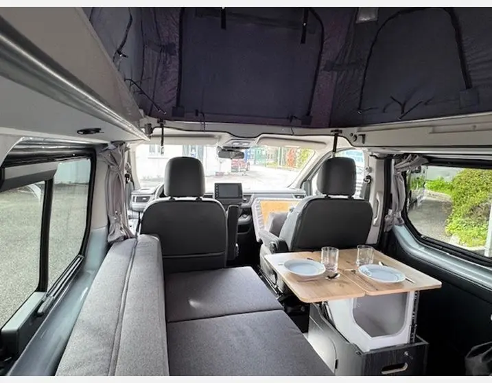 Intérieur du Renault Trafic Fourgon gris Highland, vue avant avec banquette, table et toit relevable ouvert