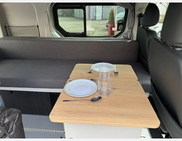 Intérieur du Renault Trafic Fourgon gris Highland, vue latérale sur la banquette et la table avec vaisselle posée.