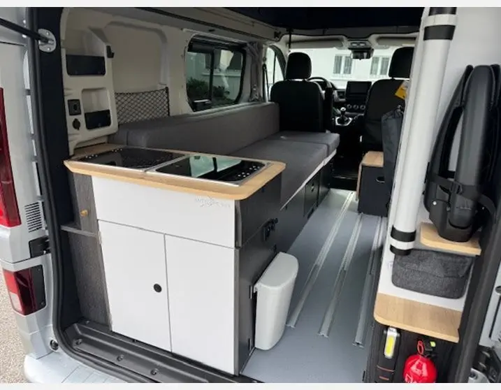 Intérieur aménagé du Renault Trafic Fourgon gris Highland, vue depuis l'arrière avec cuisine et banquette intégrées.