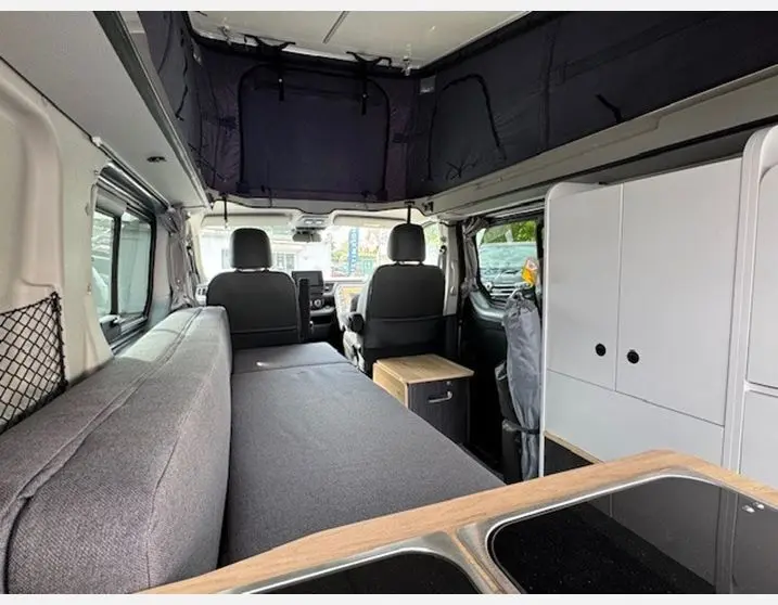 Intérieur du Renault Trafic Fourgon gris Highland, vue avant depuis l'arrière, aménagé avec banquette, cuisine et toit relevable.