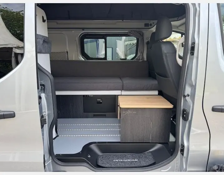 Vue intérieure côté droit du Renault Trafic Fourgon gris Highland aménagé avec banquette grise et meuble de cuisine compact en bois clair.