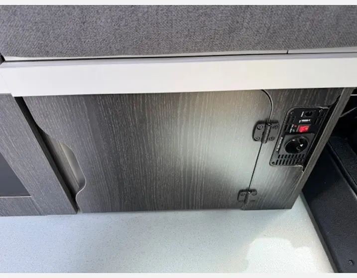 Détail du meuble bas en bois foncé avec prise électrique intégré dans l'aménagement intérieur du Renault Trafic Fourgon gris Highland.
