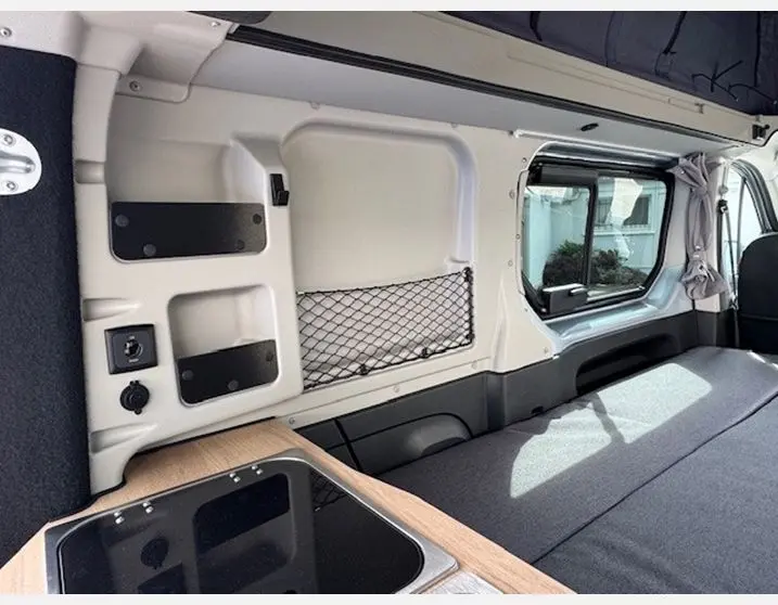 Intérieur du Renault Trafic Fourgon gris Highland, vue latérale droite sur la cuisine et banquette avec fenêtre coulissante.