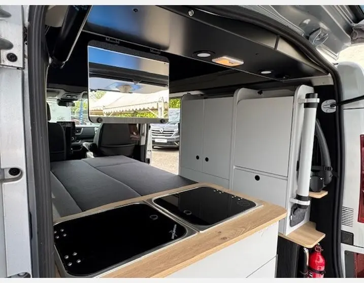 Vue intérieure arrière du Renault Trafic Fourgon gris Highland aménagé en van avec cuisine intégrée et banquette convertible.