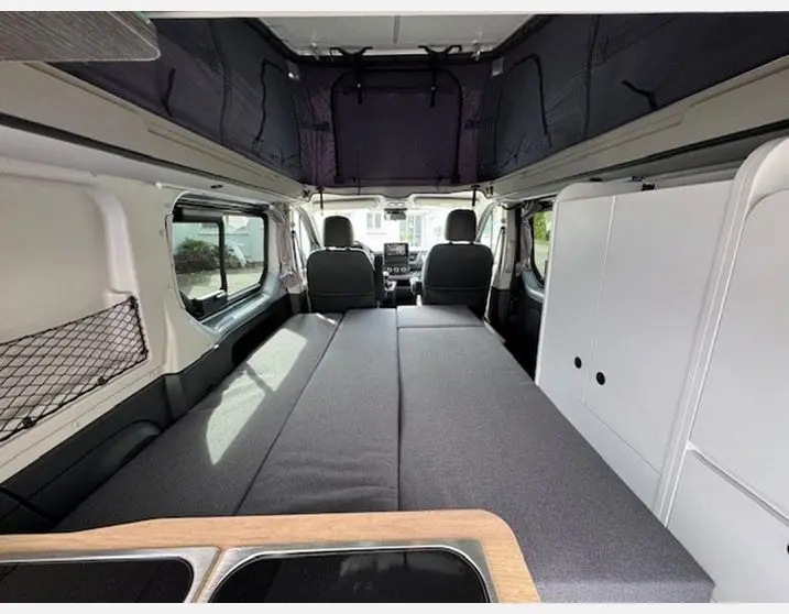Vue intérieure arrière du Renault Trafic Fourgon gris Highland, aménagé avec lit et rangements blancs intégrés.