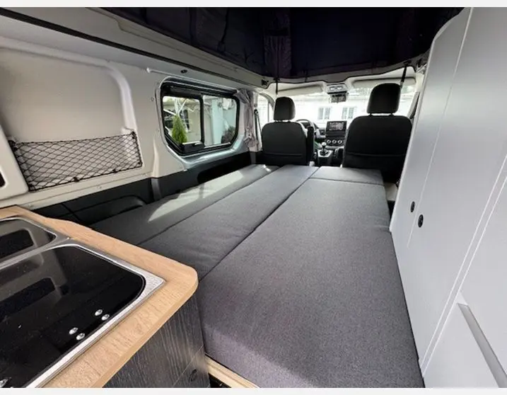 Intérieur du Renault Trafic Fourgon gris Highland, vue arrière montrant l'aménagement avec lit et cuisine intégrée.