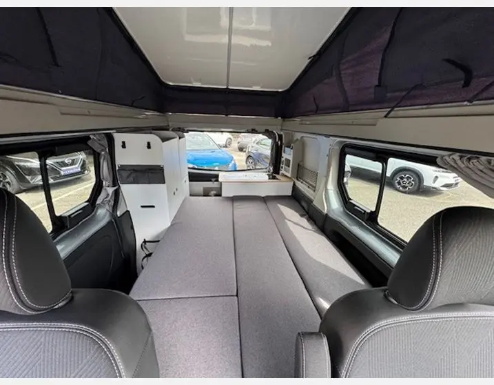 Vue intérieure arrière du Renault Trafic Fourgon aménagé avec banquette grise et toit relevable ouvert.