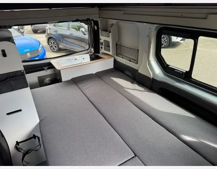 Intérieur du Renault Trafic Fourgon gris Highland, vue sur la banquette-lit et kitchenette côté droit avec fenêtres coulissantes.
