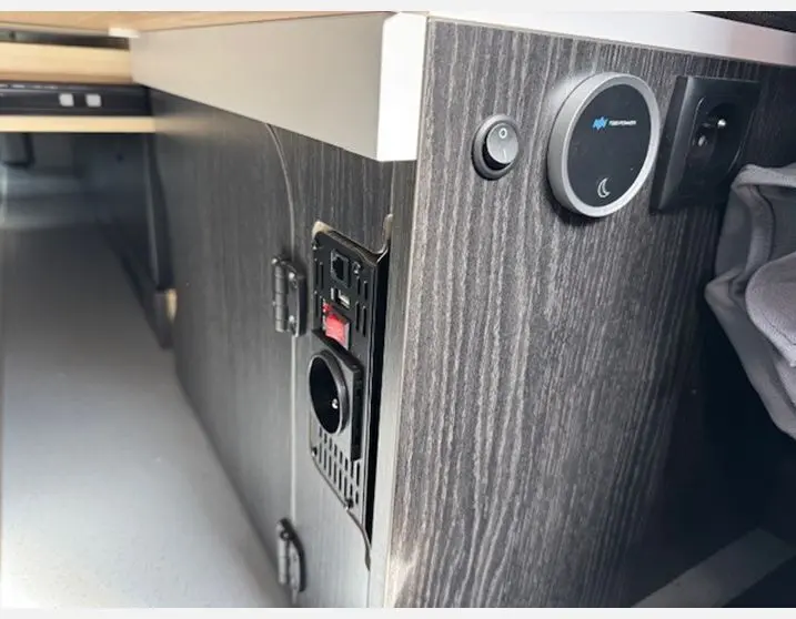 Détail du meuble bas en bois foncé avec prises électriques et interrupteur dans l'aménagement intérieur du Renault Trafic Antilope Van Flex Plus.