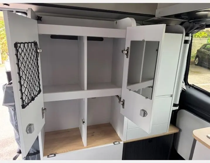 Meuble de rangement blanc ouvert avec miroir et filet, intérieur du fourgon Renault Trafic Antilope gris Highland.