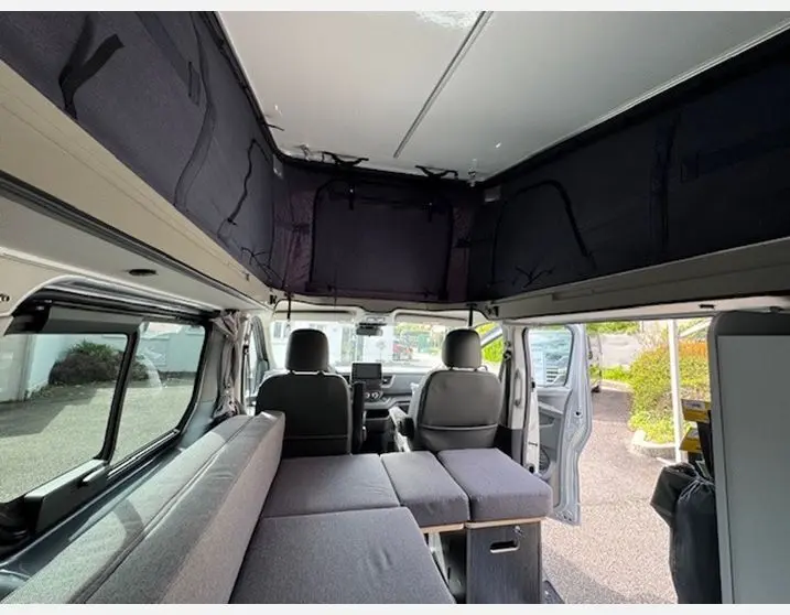 Intérieur du Renault Trafic Fourgon gris Highland 2025, vue avant avec banquette dépliée et toit relevable ouvert.