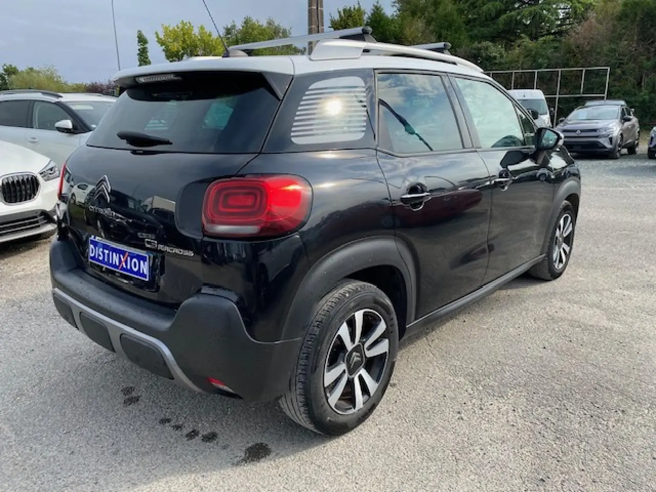 Vue 3/4 arrière droite du Citroën C3 Aircross noir avec toit blanc et jantes bicolores sur parking.