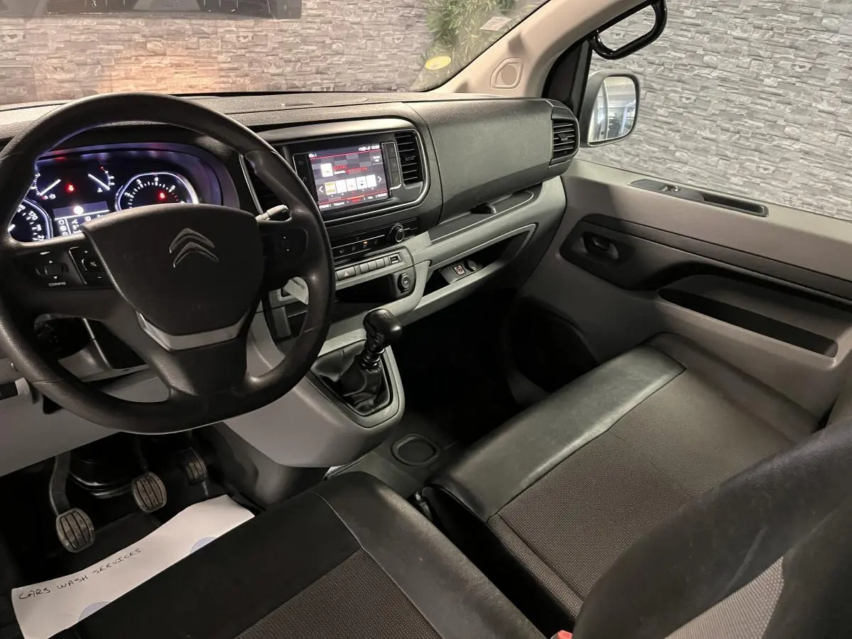 Vue intérieure côté conducteur du Citroën Jumpy blanc, tableau de bord moderne avec volant et boîte manuelle visible.