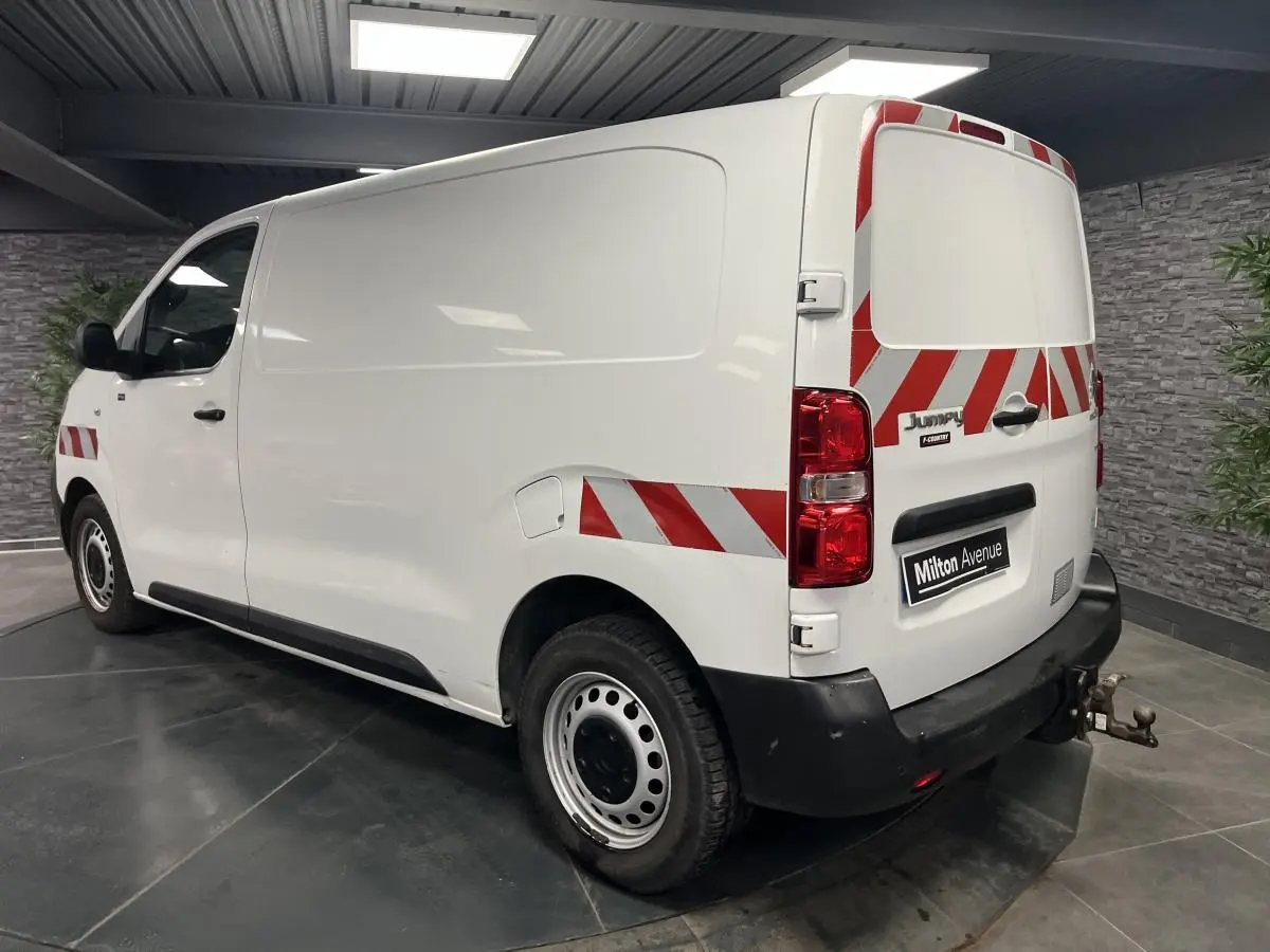 Vue 3/4 arrière droite d'un utilitaire blanc Citroën Jumpy 2019 avec bandes réfléchissantes rouges et attelage crochet.
