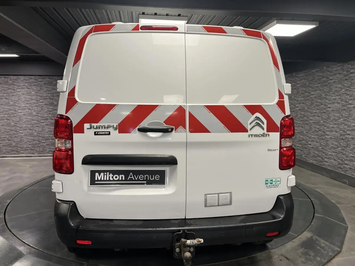 Vue arrière d'un Citroën Jumpy blanc avec bandes rouges diagonales et attelage crochet mixte visible.