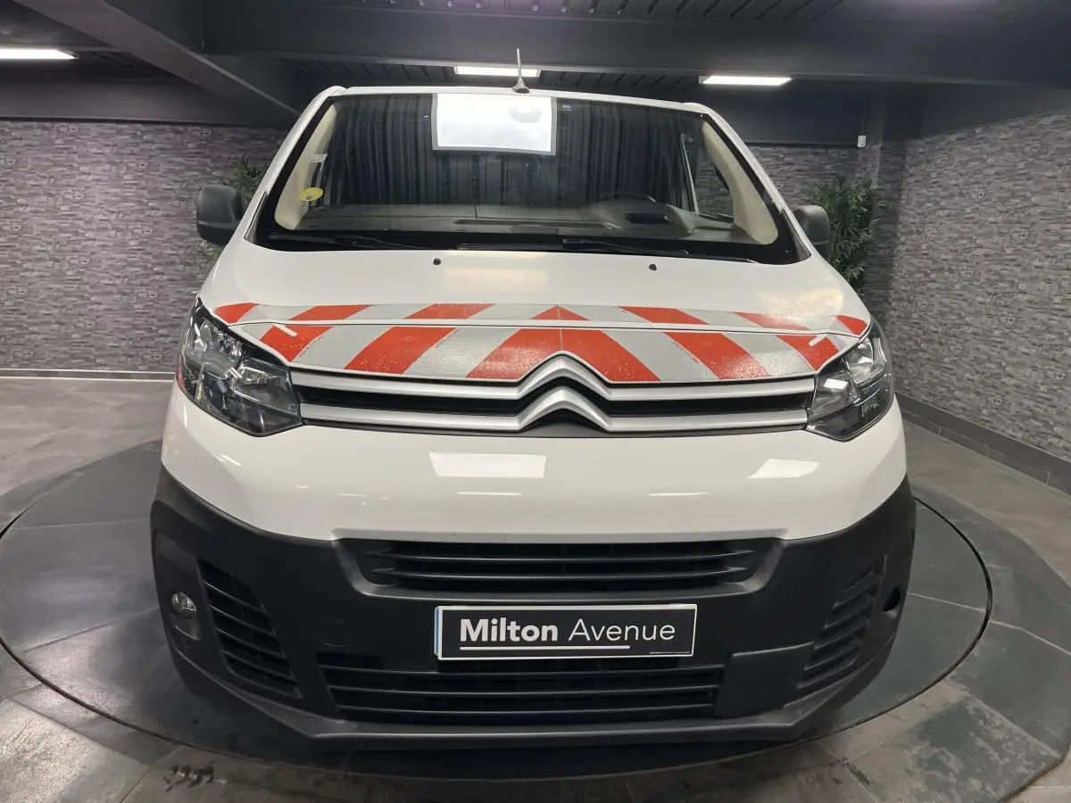 Vue frontale d'un Citroën Jumpy blanc avec bandes rouges réfléchissantes sur le capot et boucliers noirs.